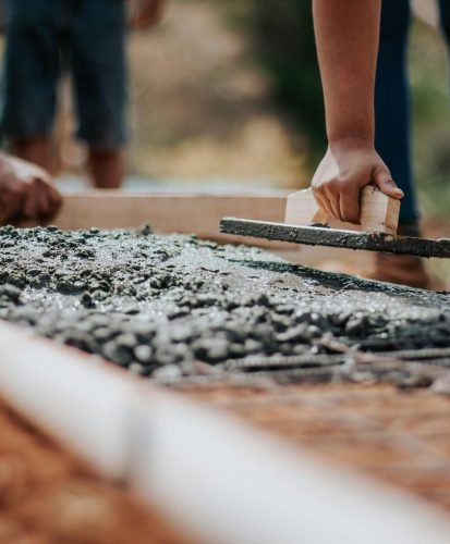 Construction workers leveling fresh cement on a sunny day at an outdoor site.
