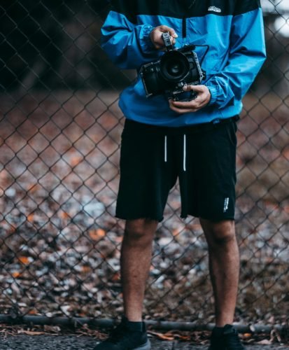 A man holding a camera stands by a wire fence, showcasing casual outdoor photography setup.