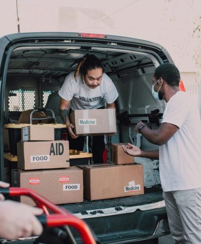 Volunteers unloading boxes labeled food and medicine from a van for charity.
